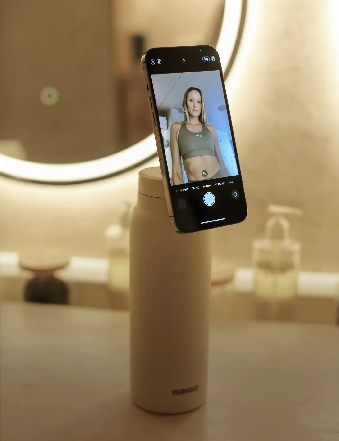 Phone on bottle in front of round mirror, reflecting a person wearing a sports outfit.