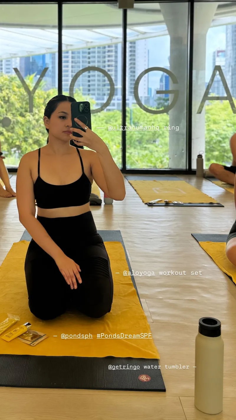 Person in yoga attire taking a mirror selfie in a yoga studio.