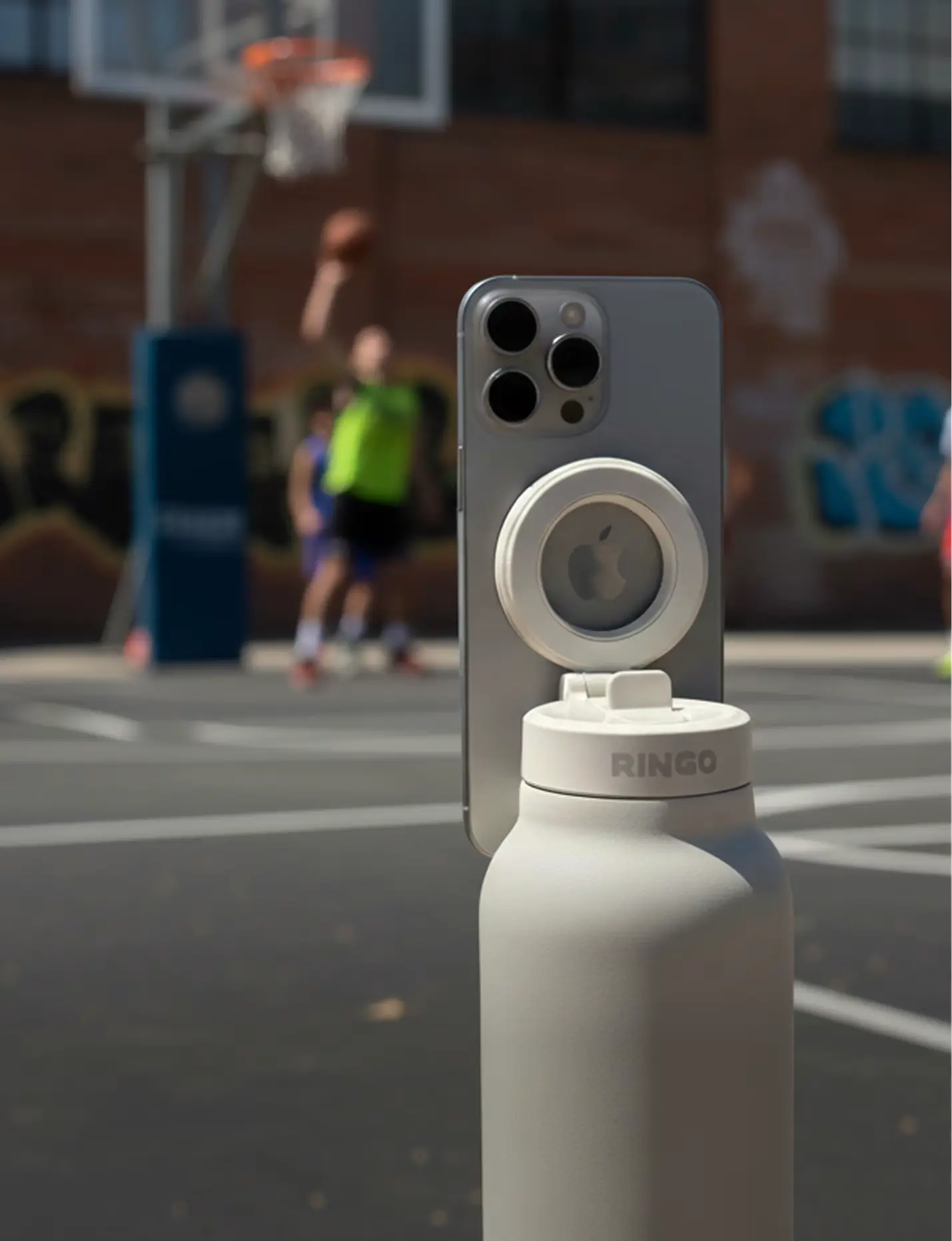 Smartphone mounted on a white water bottle at a basketball court.