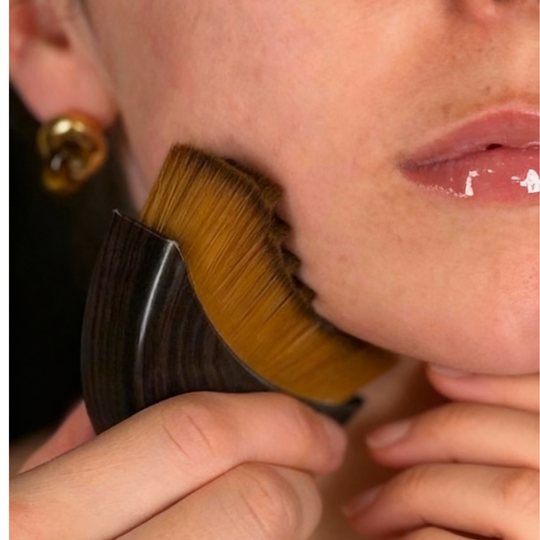 Person using a makeup brush on their jawline, applying cosmetics.