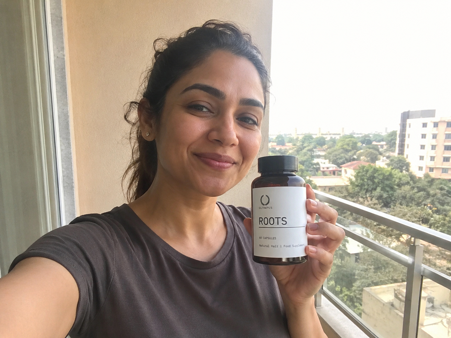 A woman with long brown hair holds up a bottle of Olympus Roots hair supplement.