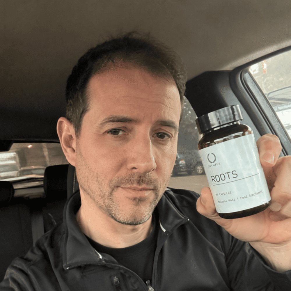 A man in a car holds up a bottle of Olympus Roots hair supplement.