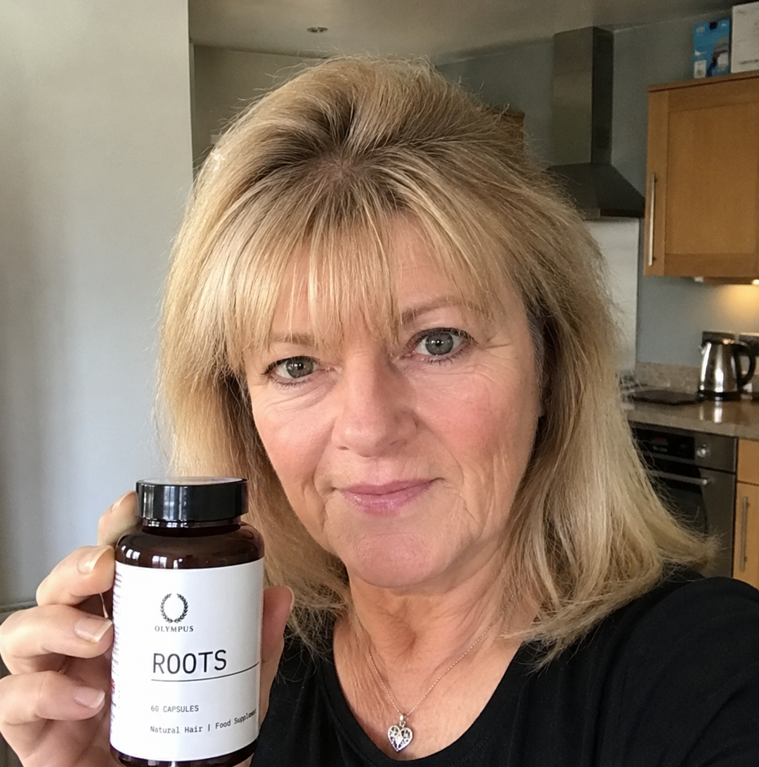 A woman with dark hair holds up a bottle of Olympus Roots hair food supplement.
