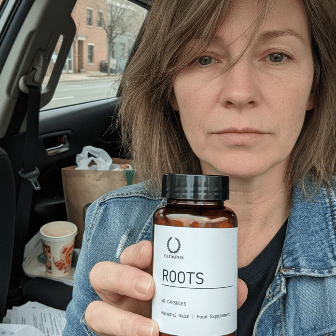 A woman in a car holds up a bottle of Oltmpus Roots natural hair food supplement.