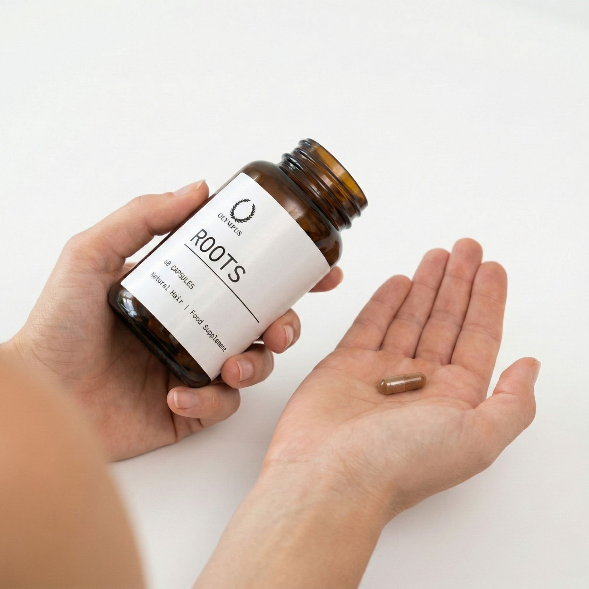 Hand holding capsule bottle labeled 'Roots' with a capsule on the palm.