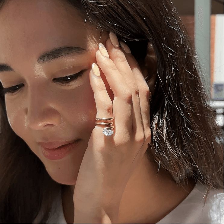Woman touching face, wearing a ring with a large gemstone.