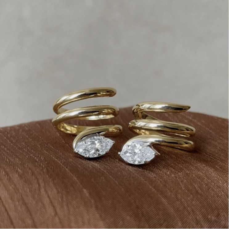 Two gold spiral rings with pear-shaped diamonds on a brown surface.