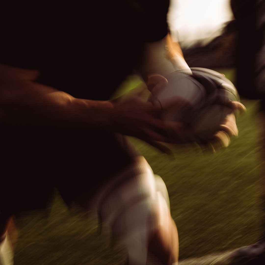 Blurred image of a person holding a rugby ball on a field.