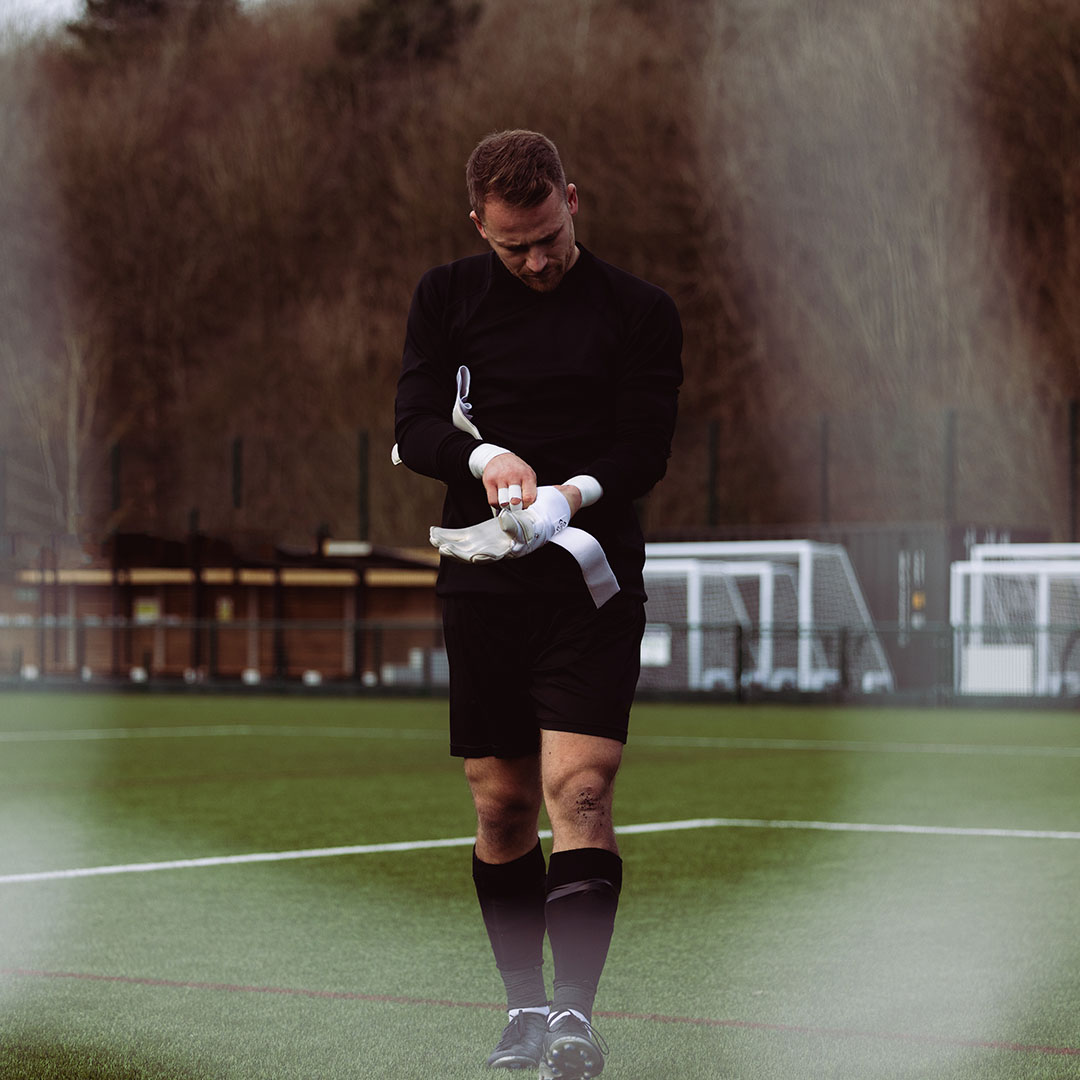 Soccer player adjusting gloves on a field with goalposts in the background.