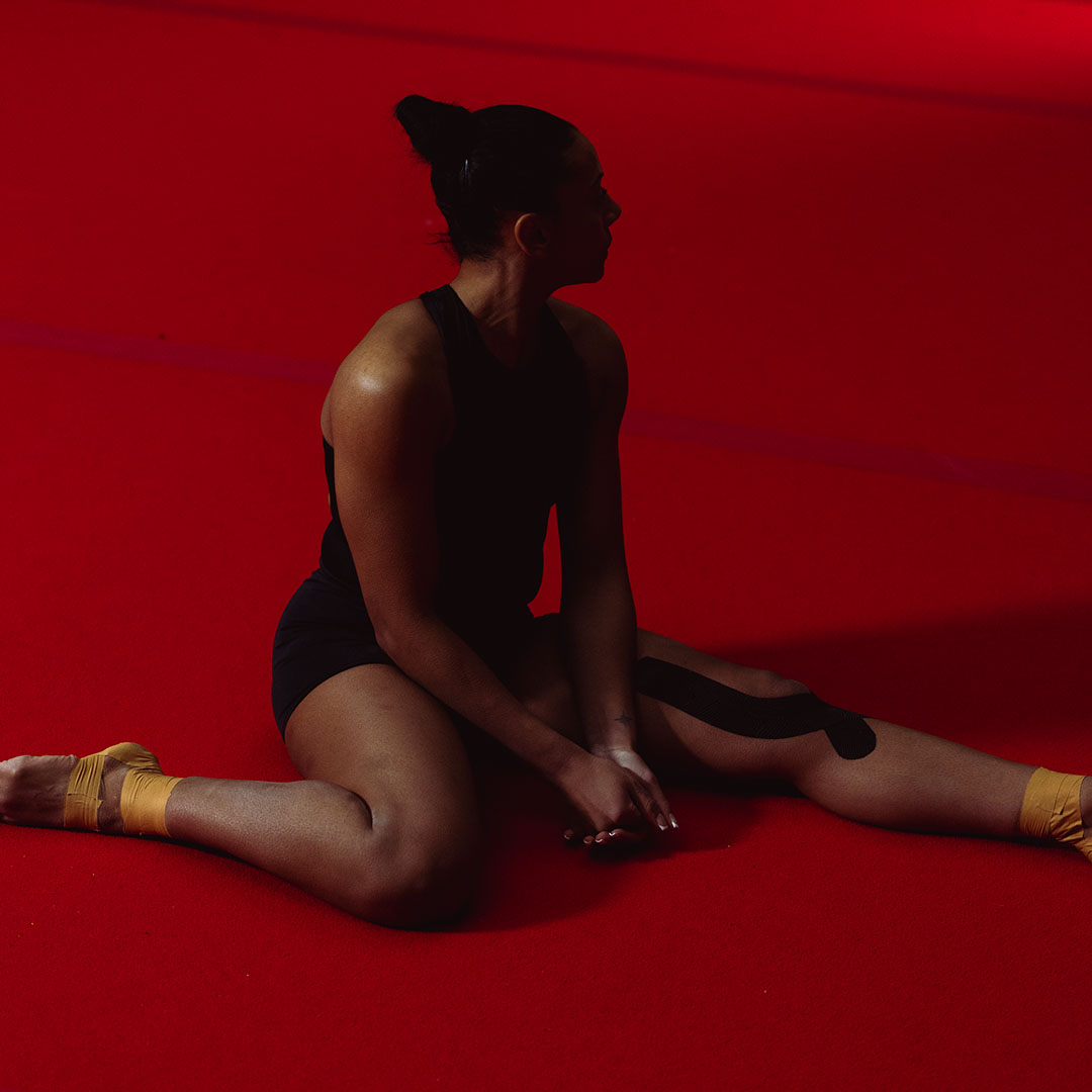 Person sitting on a red floor, wearing athletic tape and black clothing.