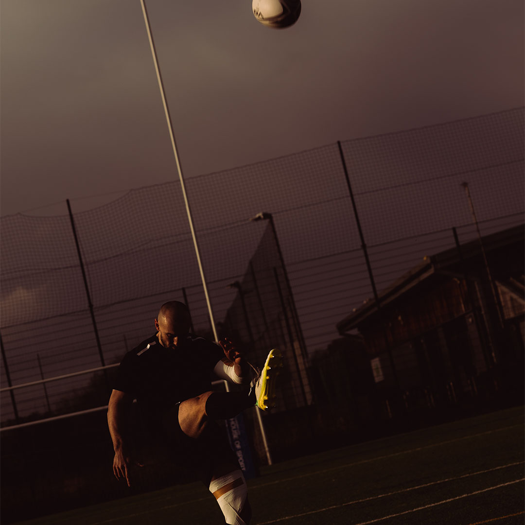 A person kicking a rugby ball on a field at dusk.