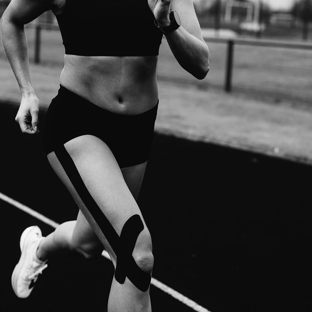 Black and white photo of a runner with knee tape on a track.