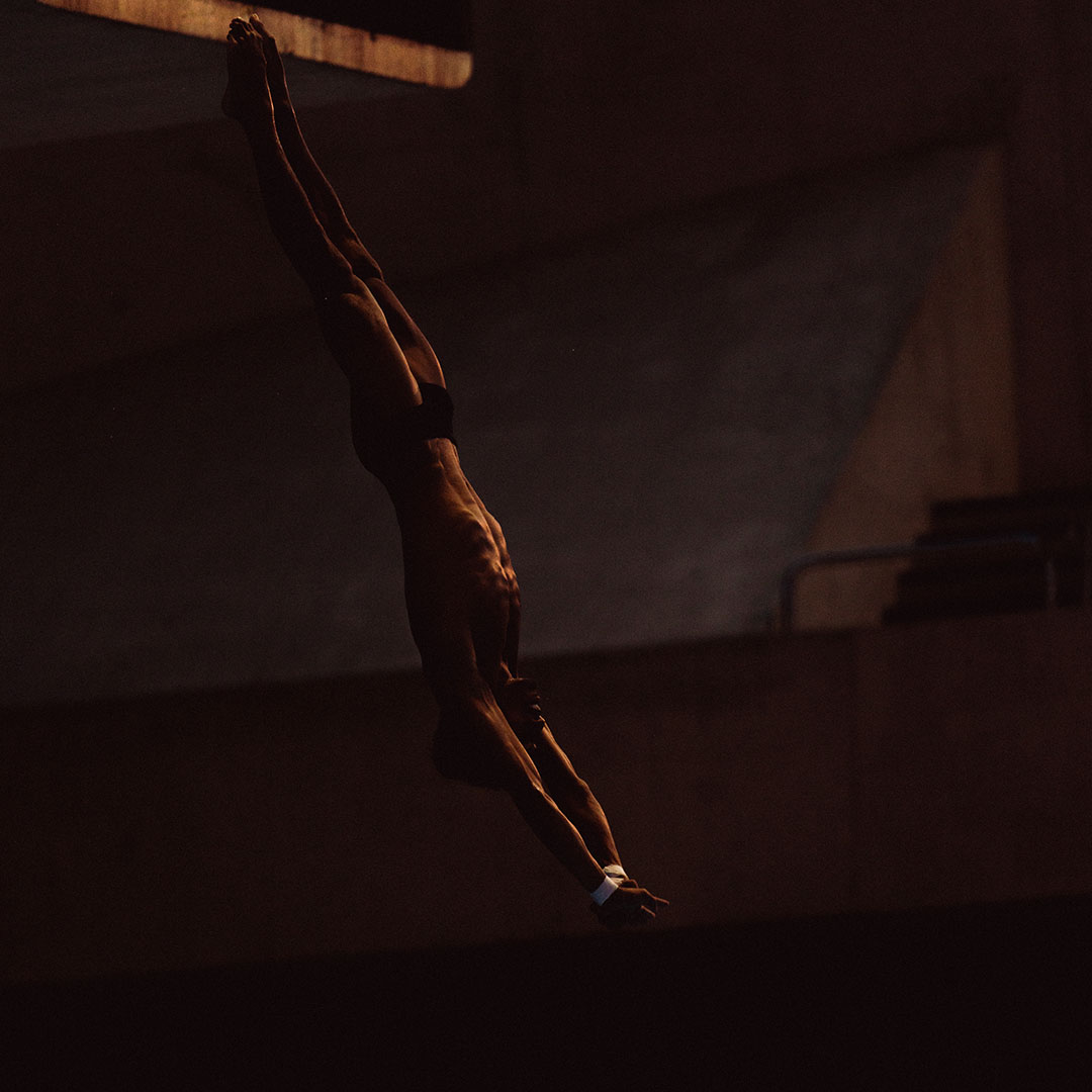 Silhouetted diver in mid-air against a dark background.
