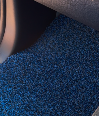 A close-up of a blue and black, noodle-textured car floor mat inside a vehicle's footwell.