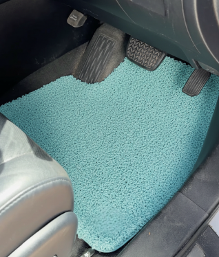 A light blue, textured car floor mat on the driver's side next to the pedals.