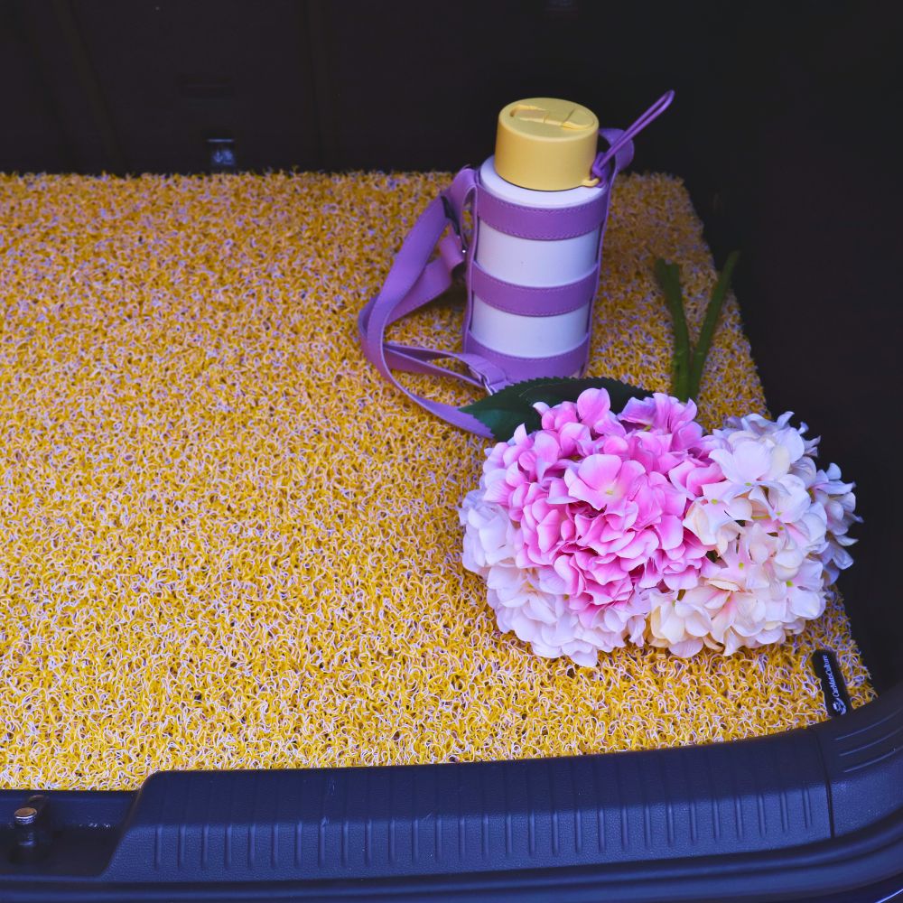 Yellow mat with flowers and a water bottle in a car trunk.