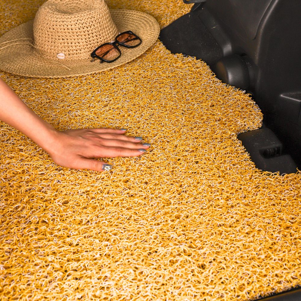 A hand touching a textured yellow mat, with a hat and glasses nearby.