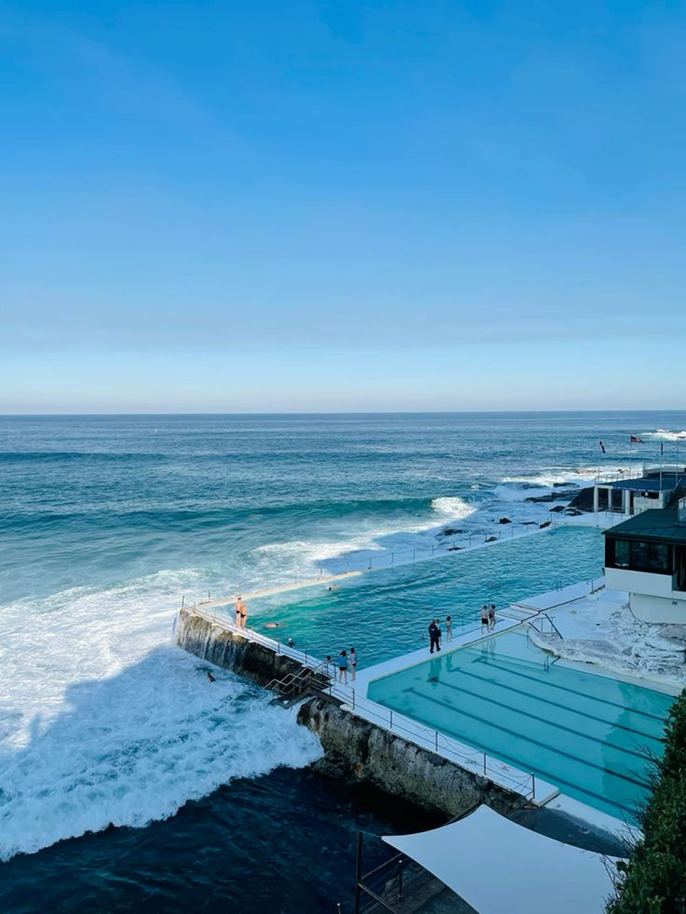 An ocean-side pool with people swimming and waves crashing nearby.