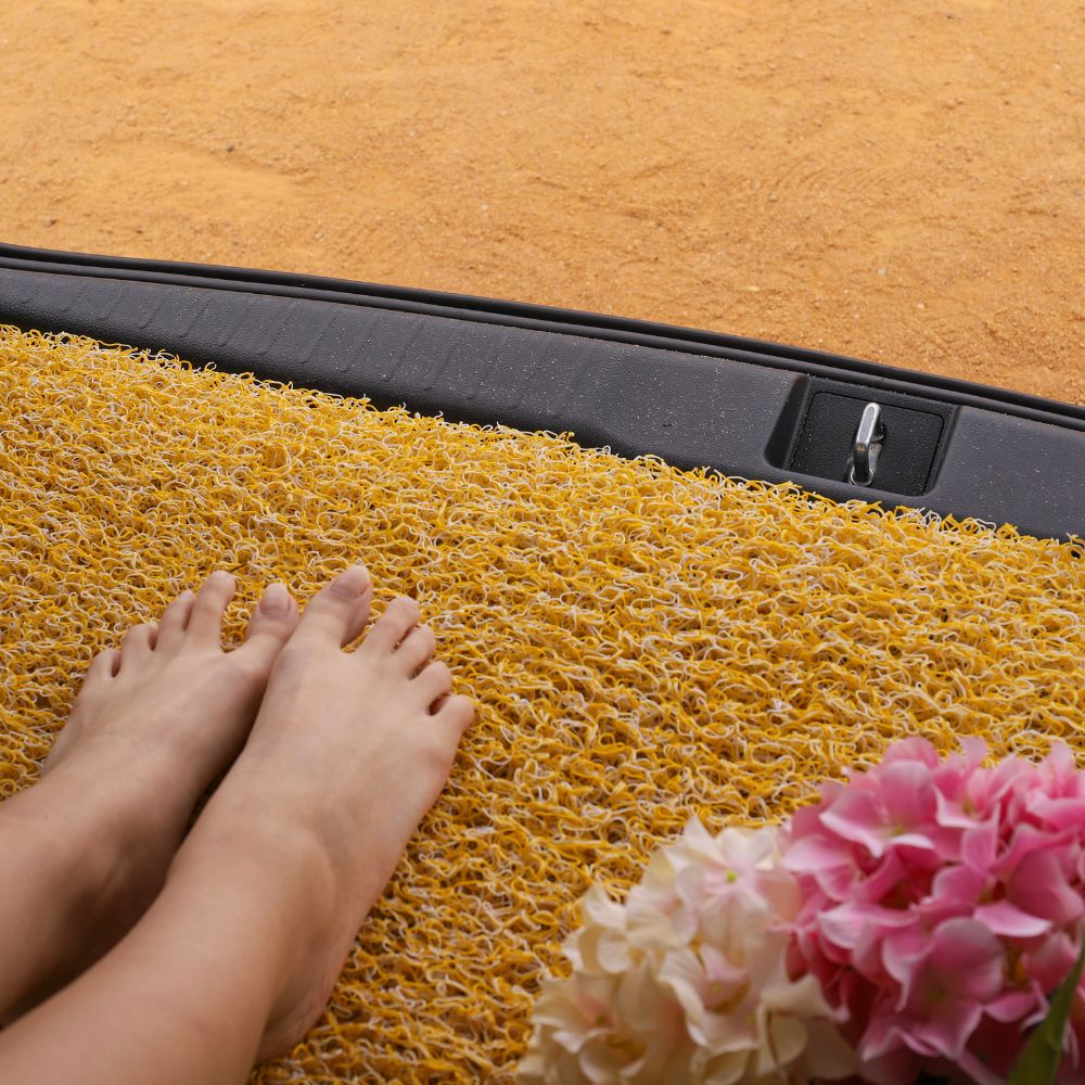 Bare feet on a yellow mat beside pink flowers.