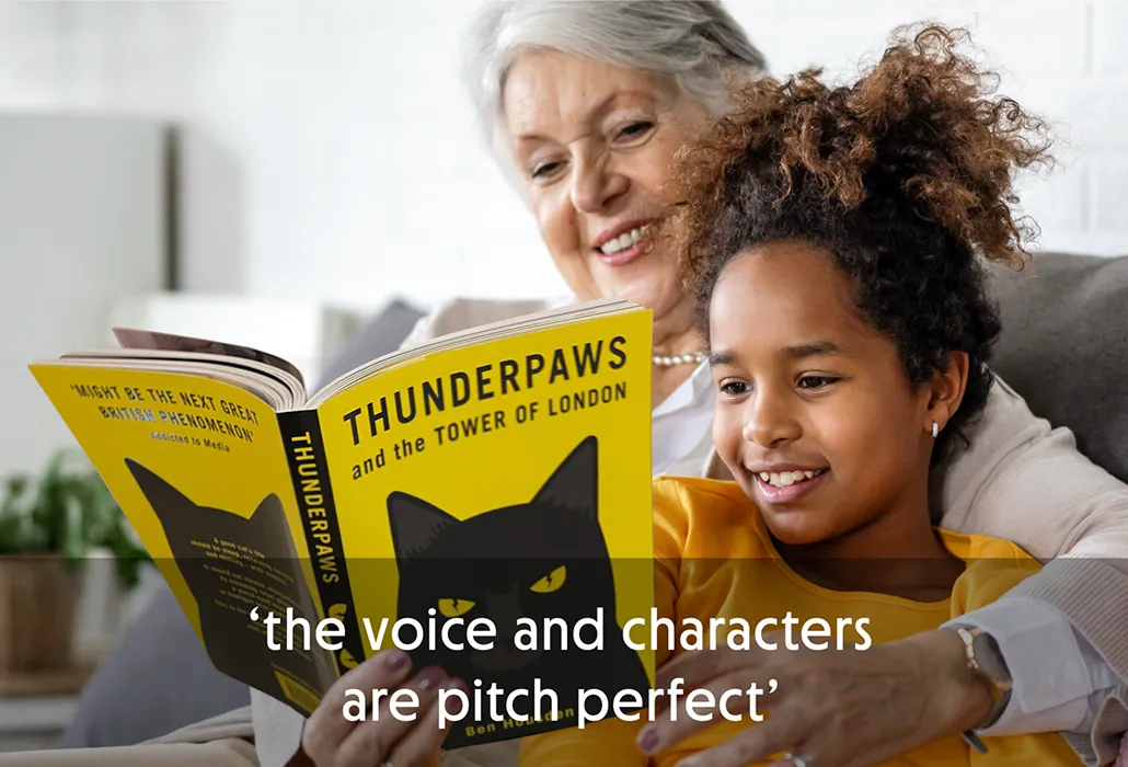 Elderly woman and a young girl on a sofa reading a book titled 'Thunderpaws and the Tower of London' with the quote “the voice and characters are pitch perfect.”