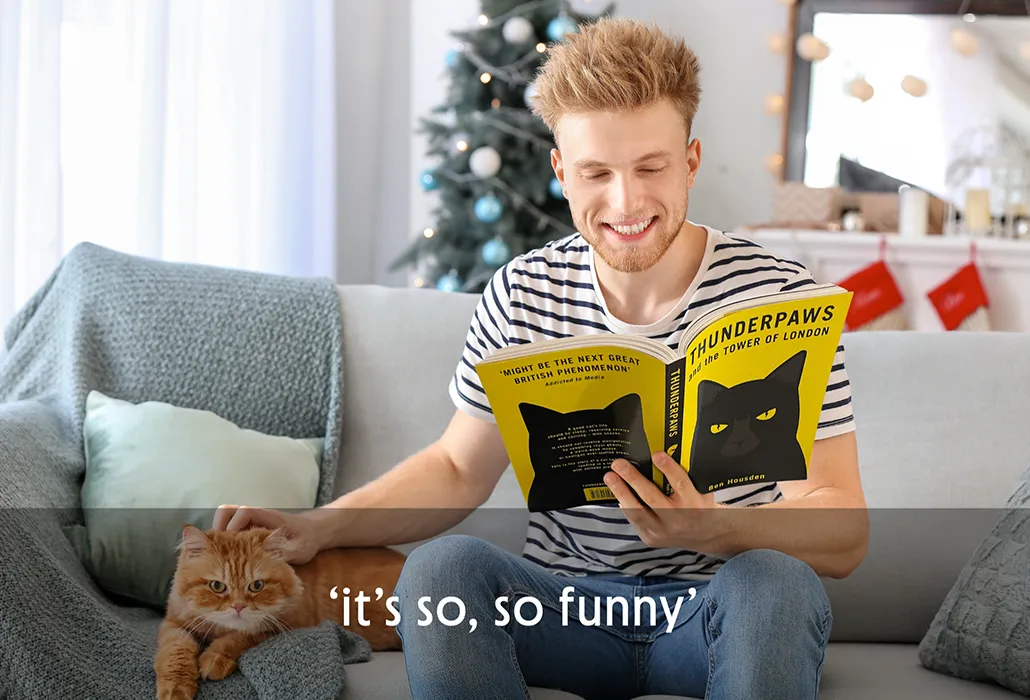Man sitting on a couch reading Thunderpaws with a grumpy ginger cat on his lap, with the quote “it’s so, so funny.”
