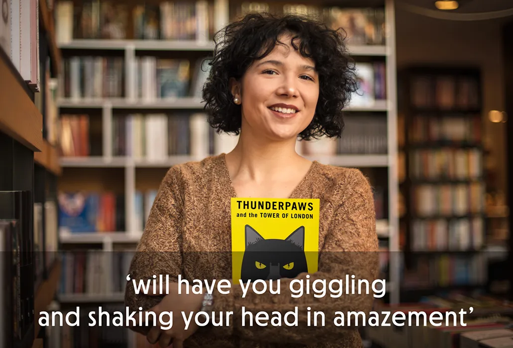 Woman in a bookshop holding a copy of 'Thunderpaws and the Tower of London' with the quote “will have you giggling and shaking your head in amazement.”