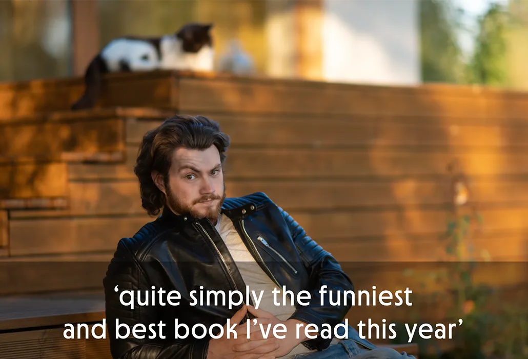 Man in leather jacket sitting outdoors with a black and white cat in the background, with the quote “quite simply the funniest and best book I’ve read this year.”