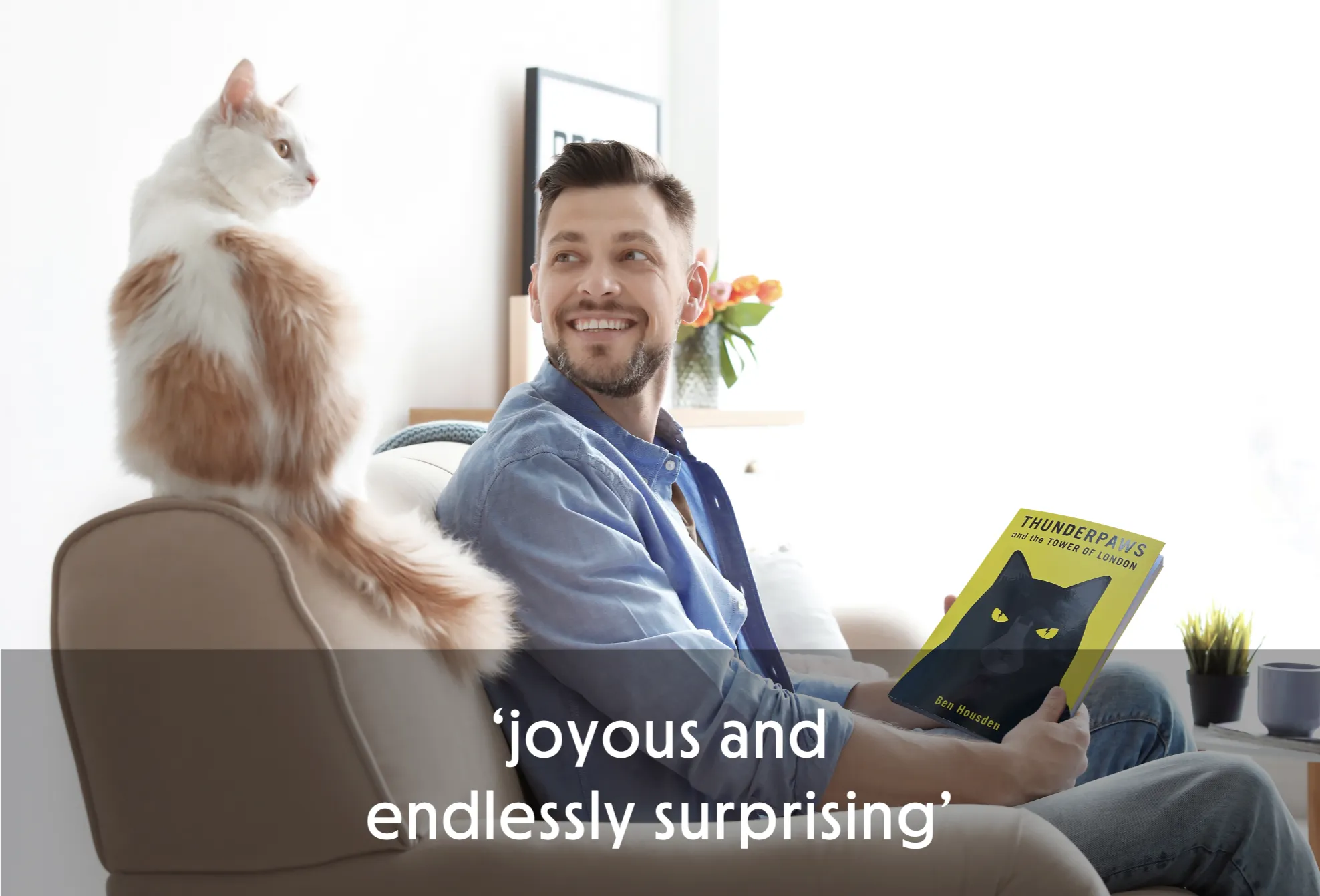 Man smiling at a cat while holding a book on a couch.