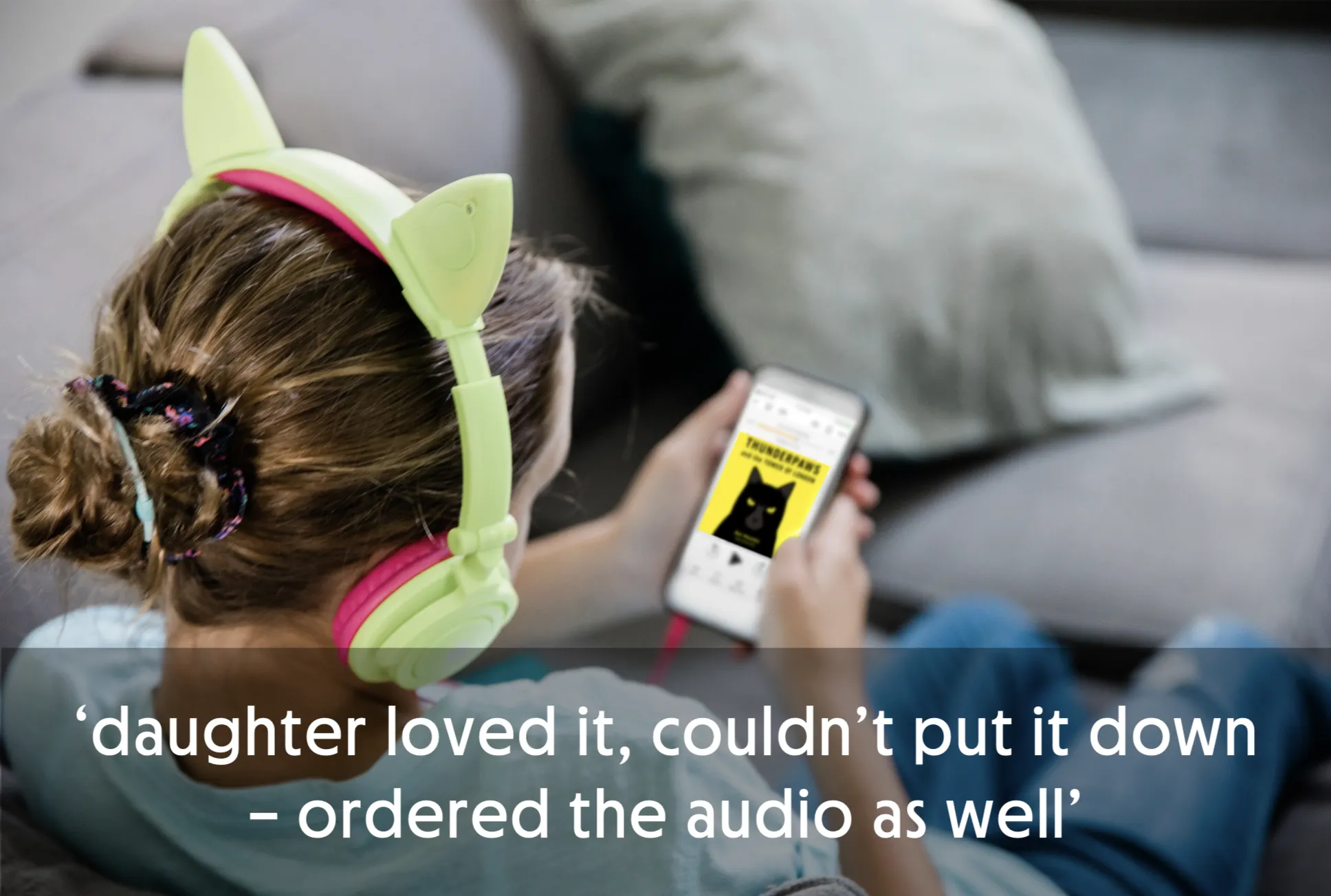 Child wearing cat ear headphones, looking at a phone with a book cover.