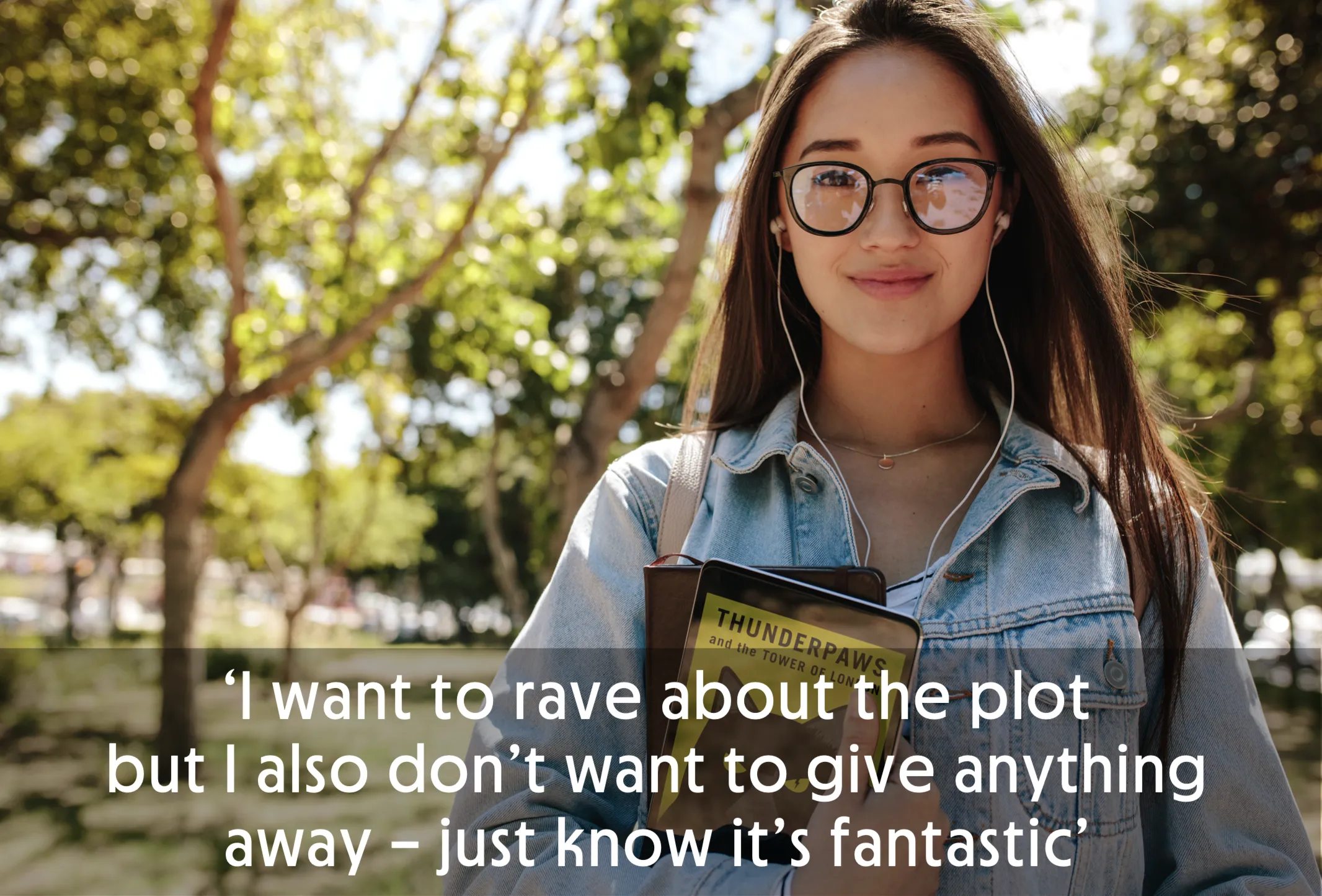 Woman with glasses holding a book, wearing earphones, standing outdoors.