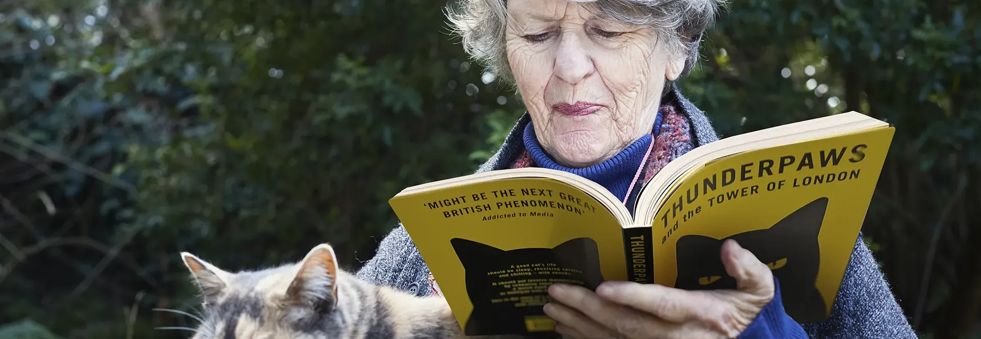 Elderly woman reading a book titled 'Thunderpaws' with a cat nearby.
