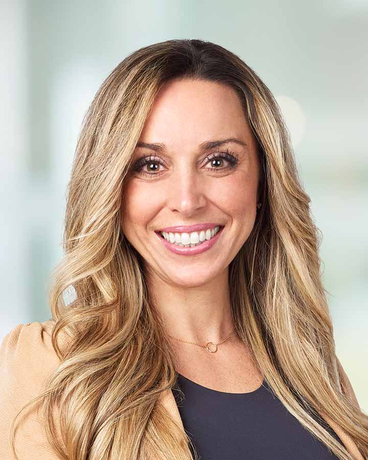 Smiling woman with long, wavy blonde hair wearing a necklace.