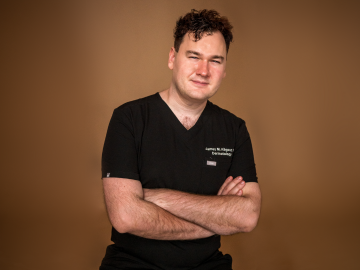 Person with crossed arms wearing a black shirt against a brown background.
