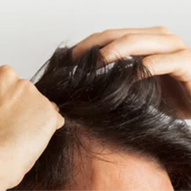 A person runs their hands through their dark hair, showing their scalp.