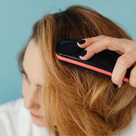A person with dark nail polish brushing their highlighted blonde hair with a black and red brush.
