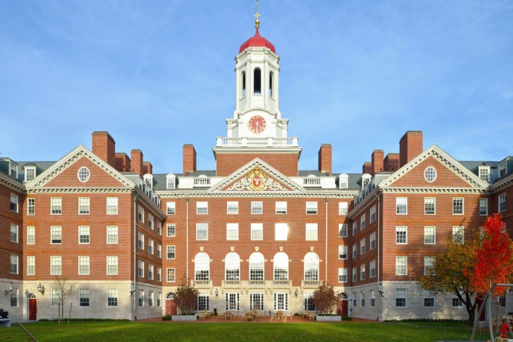 A large, symmetrical red brick building with a central clock tower and red dome, viewed from a lawn.
