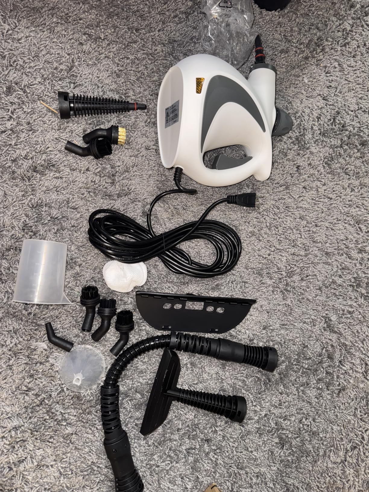 Steam cleaner with various attachments on a gray carpet.