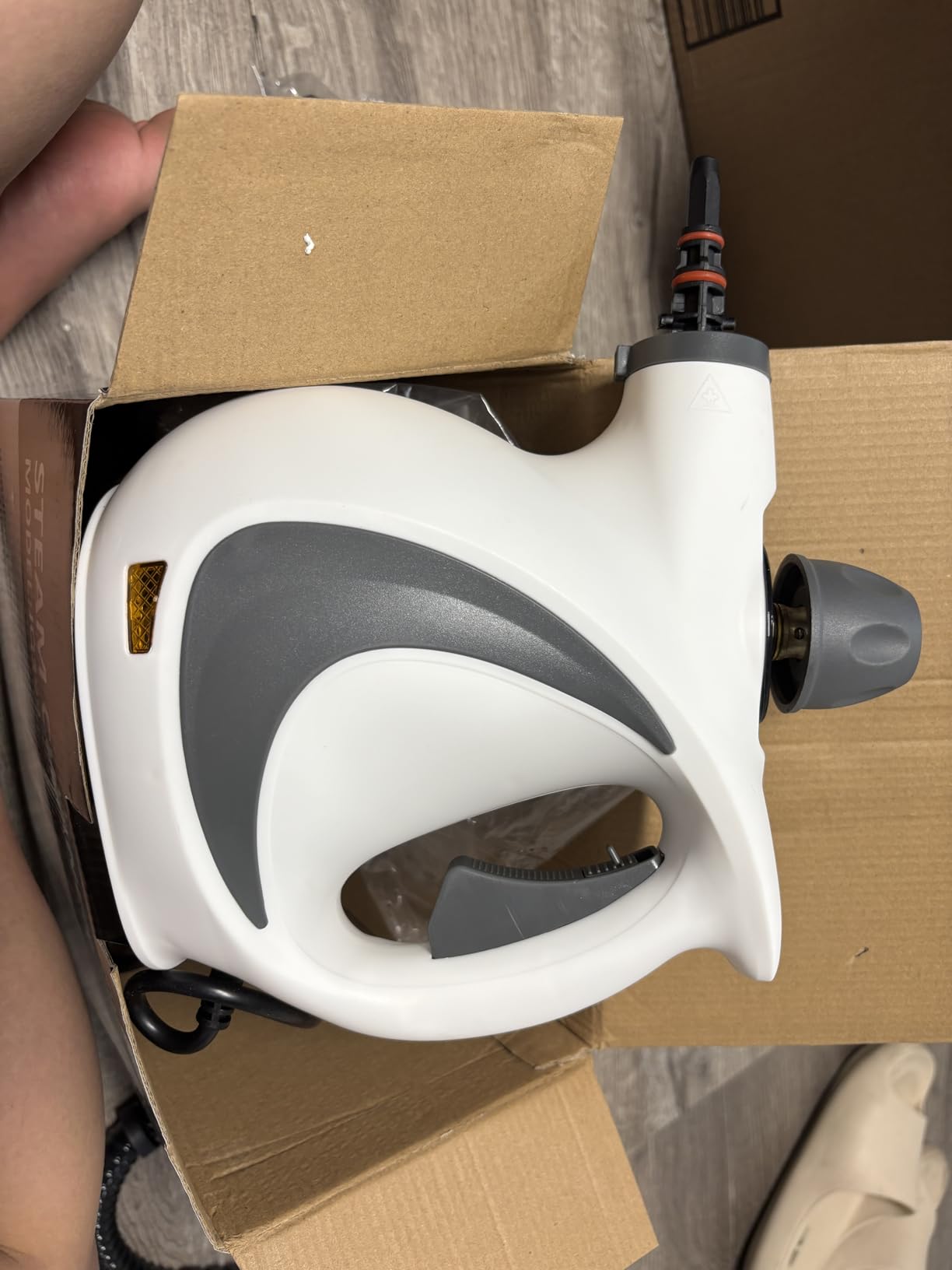 White and gray handheld steamer in an open cardboard box.