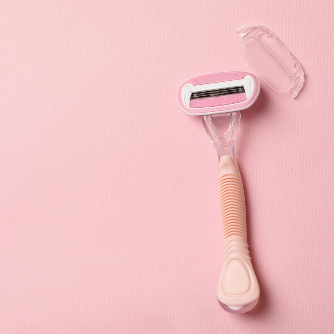 Pink plastic razor with a protective cap on a pink background.