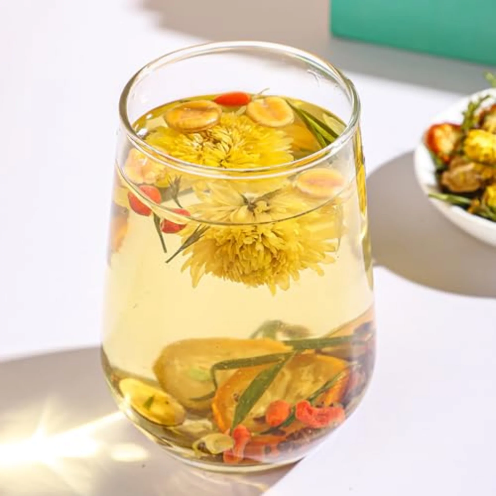 Glass of herbal tea with floating flowers and fruits.