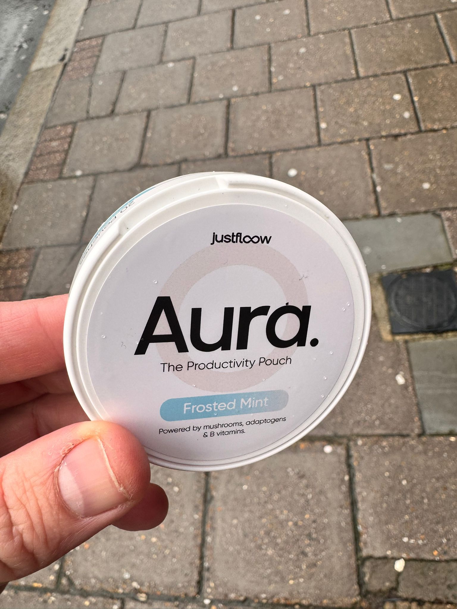 A hand holding a white tin of Justflow Aura, The Productivity Pouch, in Frosted Mint flavor.
