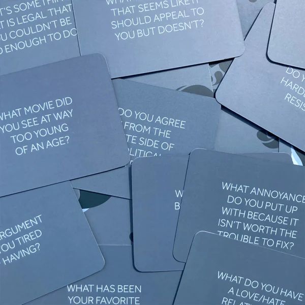 A pile of grey cards with conversation-starting questions printed on them in white text.