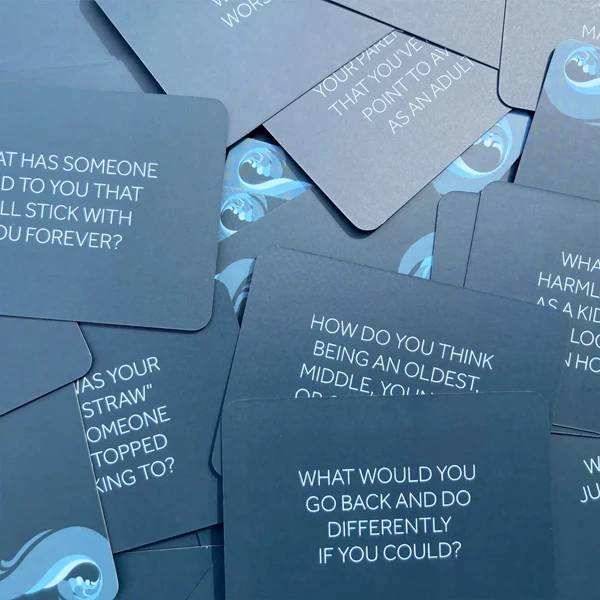 A pile of grey-blue cards with conversation-starting questions printed on them, fanned out on a surface.