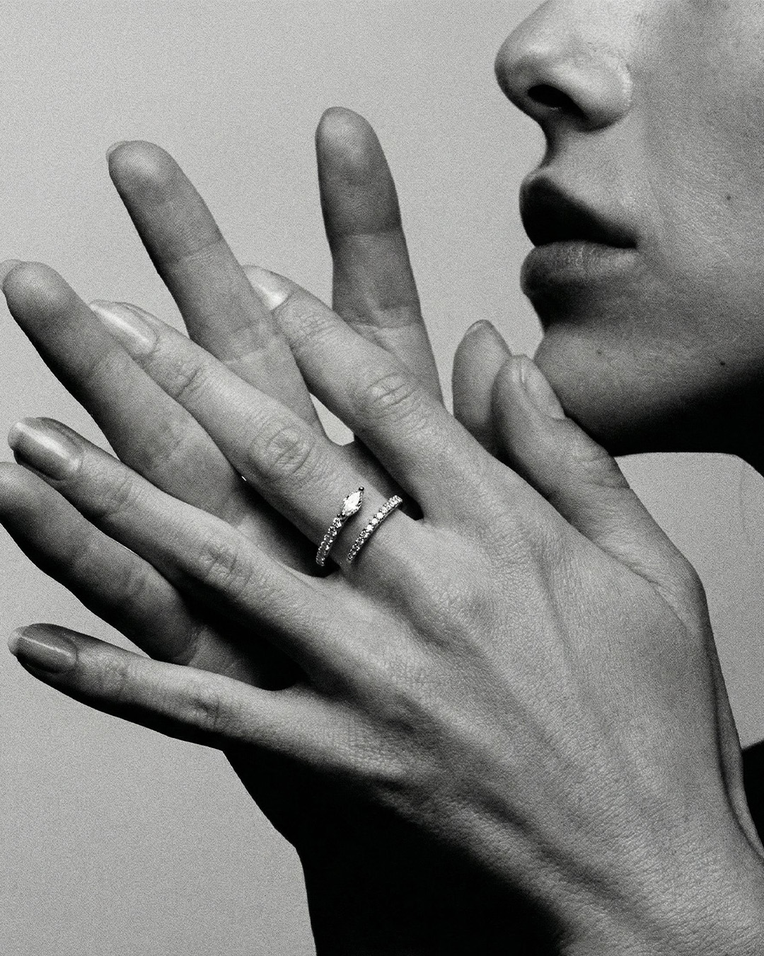 A black and white close-up of a person's hands, wearing a diamond ring, held near their face.