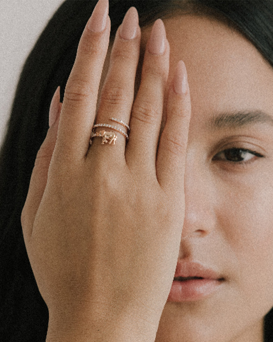 A woman holds her hand with a gold spiral ring over one eye, partially obscuring her face.