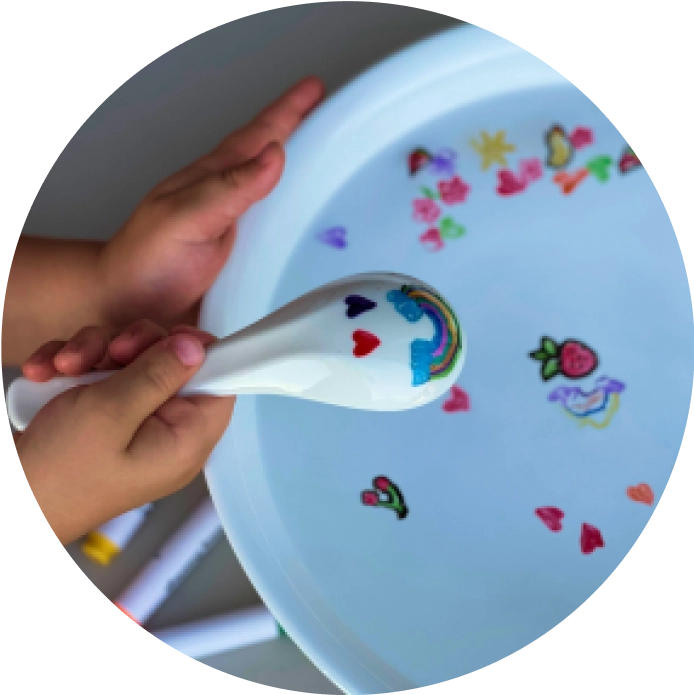 Child's hands holding a spoon with colorful drawings on a white plate.
