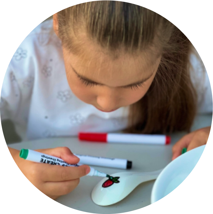 Child drawing on a ceramic spoon with markers.