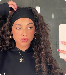 Person with curly hair taking a mirror selfie, wearing a black headband and hoodie.