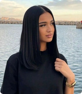 Person with long black hair standing by the water, wearing a black shirt.