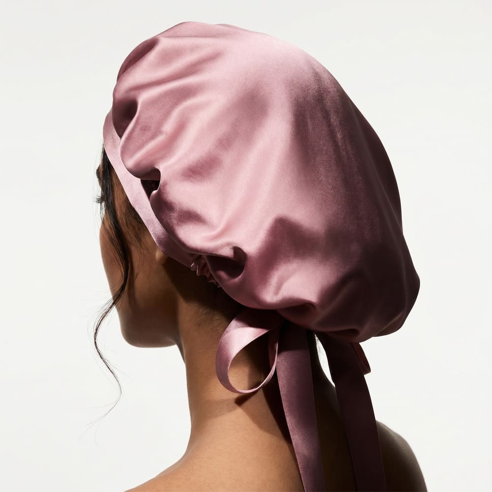 The back of a person's head wearing a large, pink satin bonnet with a ribbon tie.